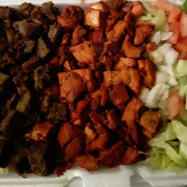 Close-up of chopped dark meat, red chicken, and fresh salad in a takeout container.