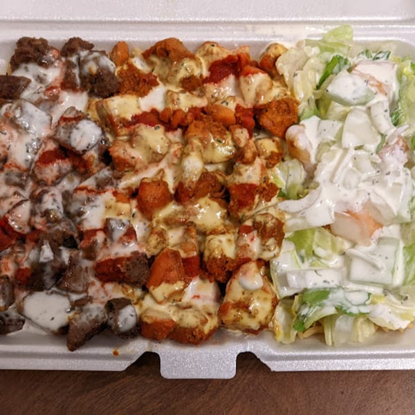 Halal platter with beef, chicken, and salad, all drizzled with white and yellow sauces.